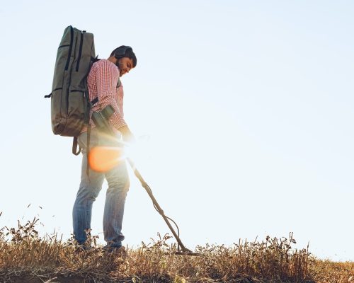 Man with metal detector equipment searching for metal goods in the field